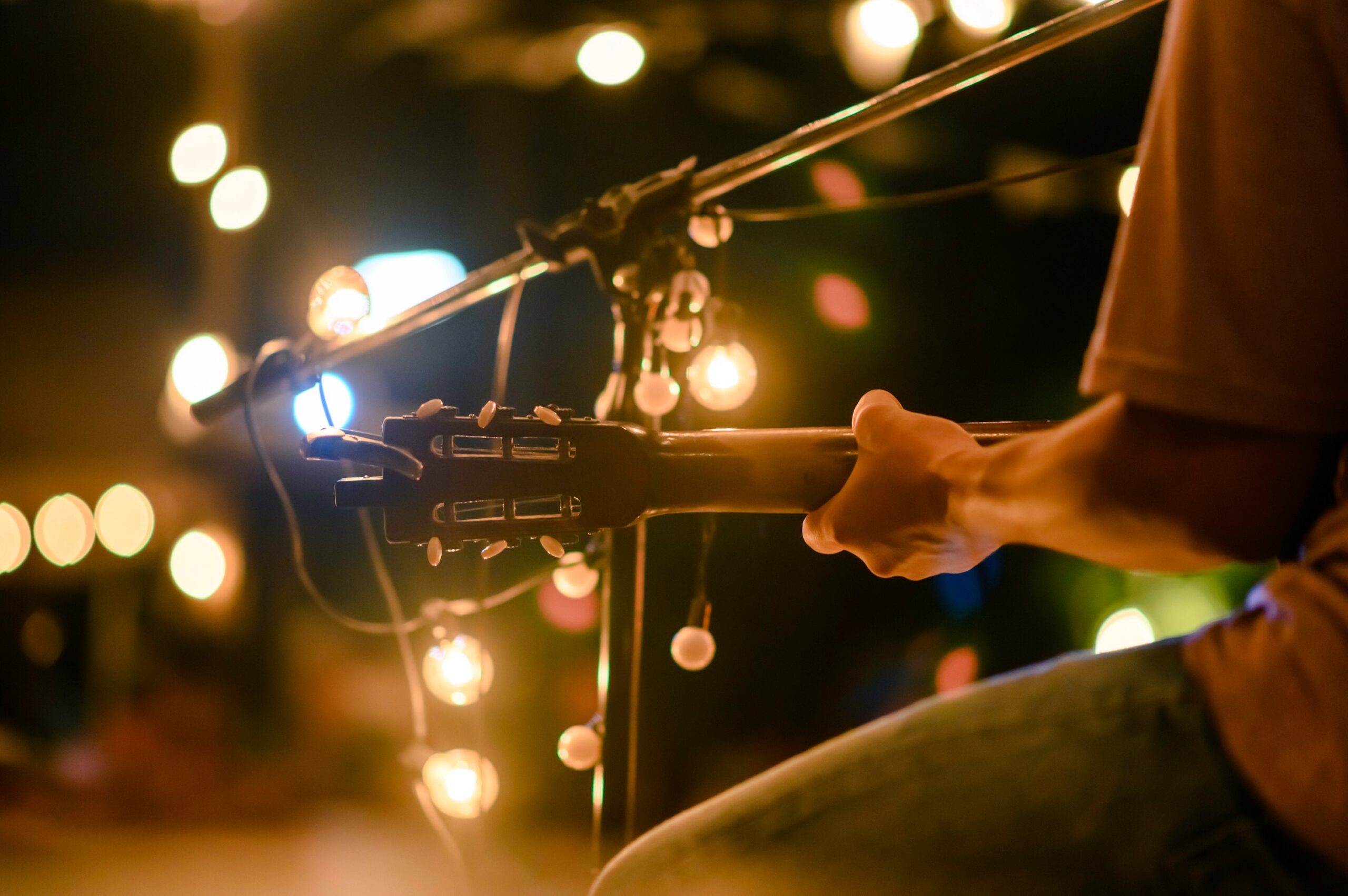 Close up of a musician playing an acoustic guitar during an outdoor evening concert with warm bokeh string lights scaled