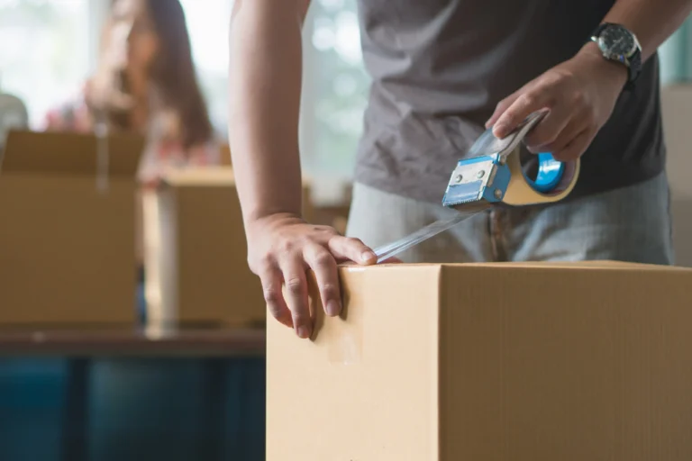Close up of a person using a tape dispenser to seal a cardboard box for moving or packing