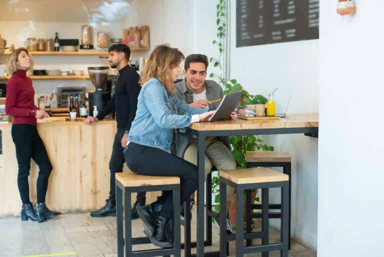 Young adults working together on a laptop at a high top table inside a coffee shop
